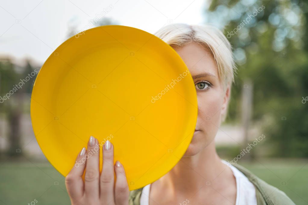 beautiful blonde woman holding yellow flying disk and looking at camera