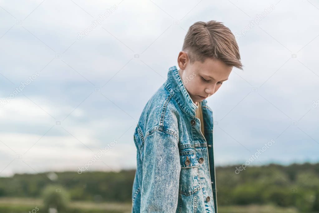 beautiful boy in denim jacket looking down at cloudy day