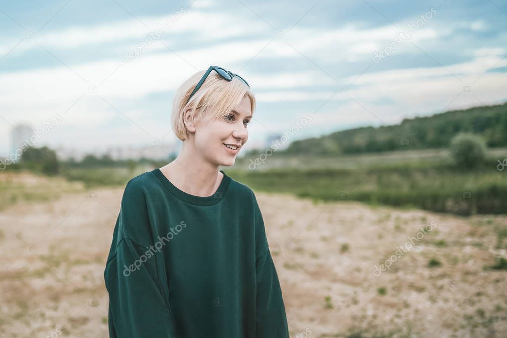 smiling blonde woman with sunglasses on head looking away while standing outdoors