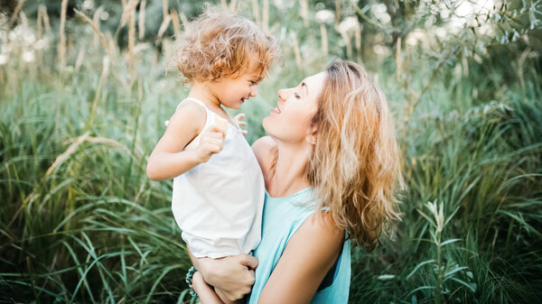 side view of smiling mother holding adorable child in green grass