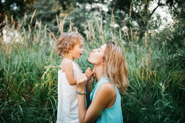 side view of mother going to kiss daughter and squatting in grass