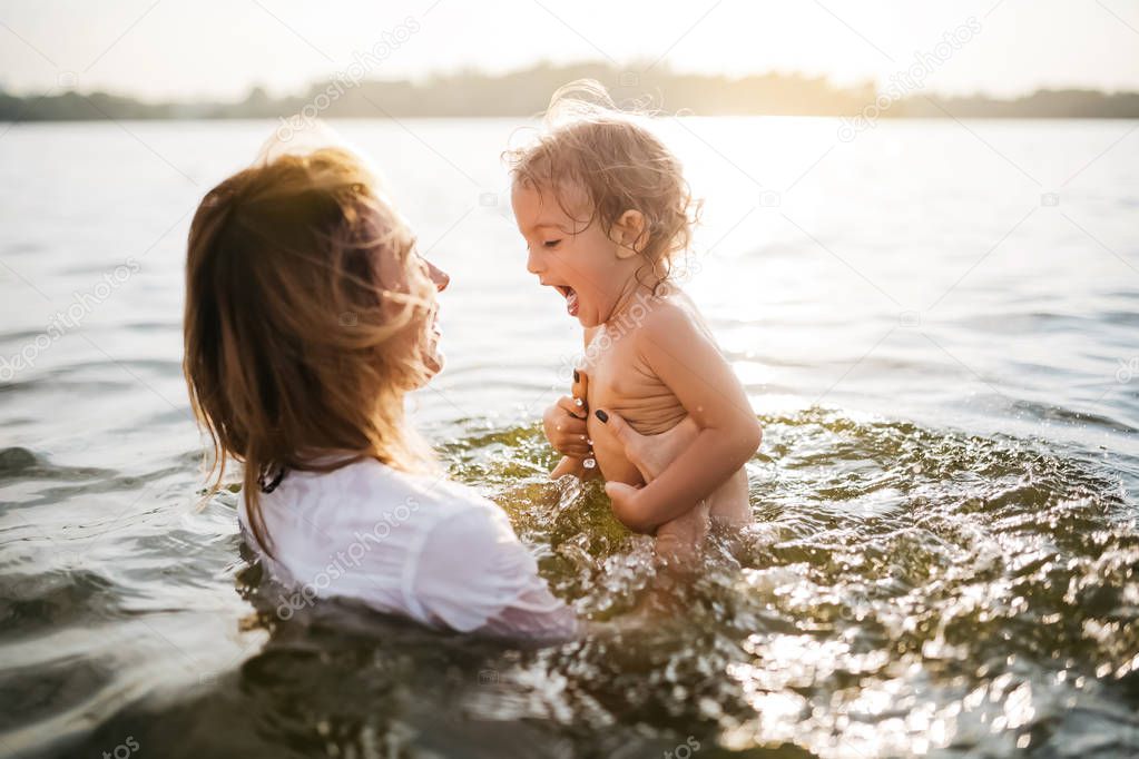happy mother holding screaming daughter in river