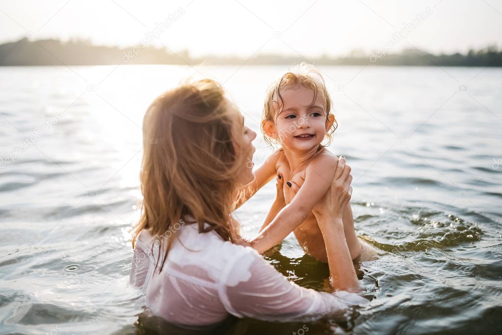 mother holding happy daughter in river during sunset