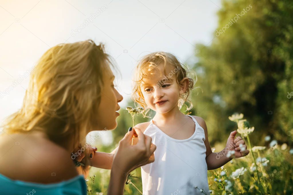 mother sniffing field flowers, smiling daughter looking at mom
