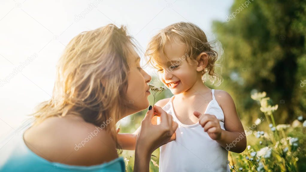mother sniffing field flowers near daughter