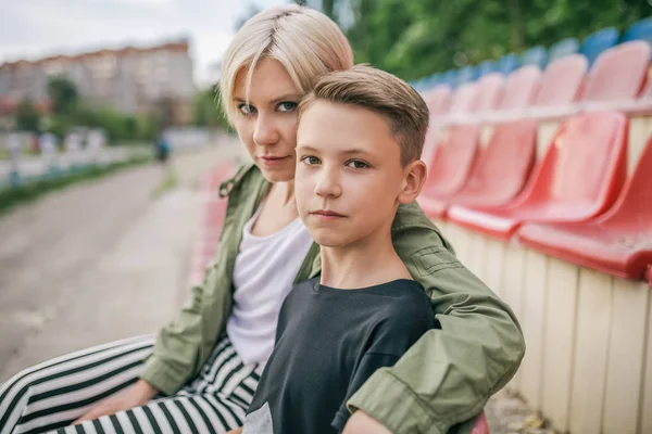 Belle mère et fils regardant la caméra tout en étant assis ensemble sur les sièges du stade — Photo de stock