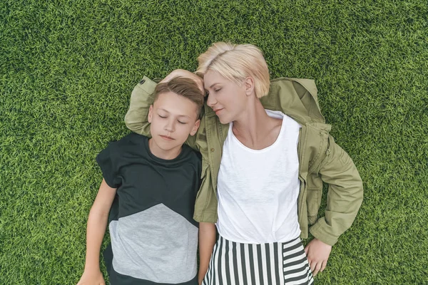 Vue de dessus de la belle mère et le fils avec les yeux fermés couchés ensemble sur la pelouse verte — Photo de stock