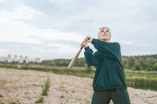 Schöne blonde Frau spielt mit Baseballschläger und blickt in den bewölkten Himmel — Stockfoto