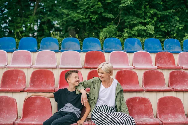 Madre e figlio felici che si sorridono mentre si siedono insieme sui sedili dello stadio — Foto stock
