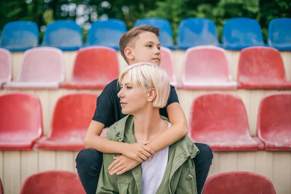 Mother and son hugging and looking away while sitting on stadium seats — Stock Photo