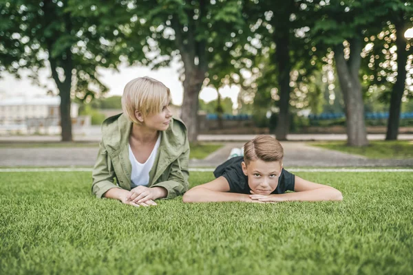 Beautiful mother and son lying together on green grass — Stock Photo