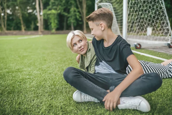 Happy mother and son smiling each other while resting together on green lawn — Stock Photo