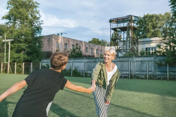 Felice madre e figlio che si tengono per mano e si sorridono mentre si divertono sul prato verde — Foto stock