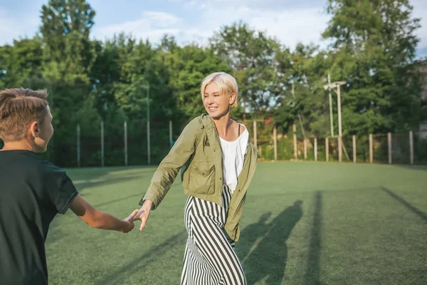 Plan recadré de mère heureuse et fils tenant la main et se souriant tout en s'amusant sur la pelouse verte — Photo de stock