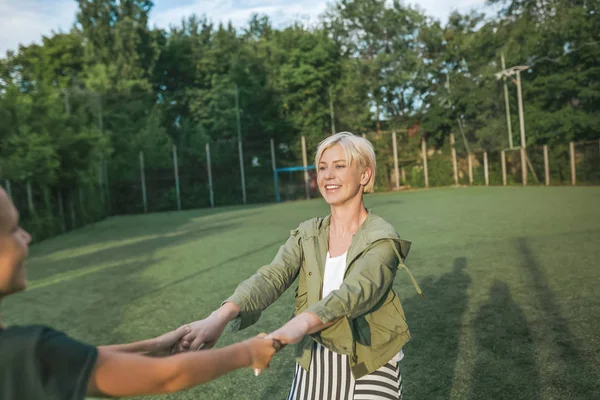 Plan recadré de mère heureuse et fils tenant la main et s'amusant sur la pelouse verte — Photo de stock