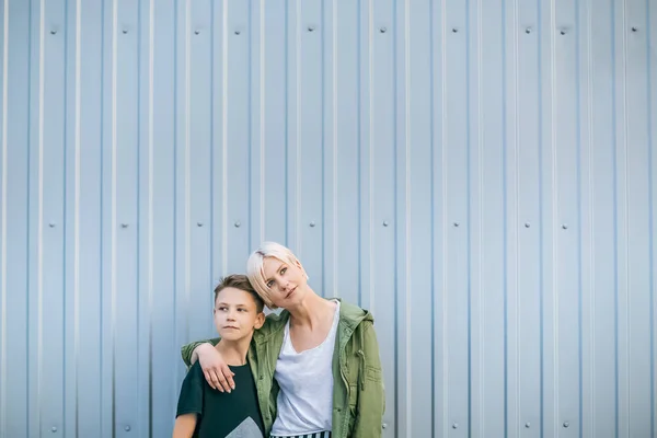 Beautiful stylish mother and son looking away while standing and embracing on street — Stock Photo