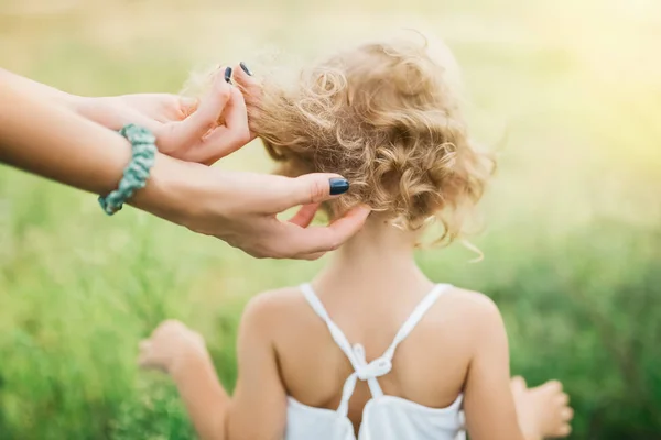 Imagem cortada da mãe tocando o cabelo encaracolado da criança ao ar livre — Fotografia de Stock