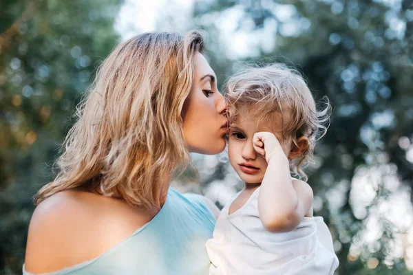 Mother kissing crying daughter outdoors — Stock Photo