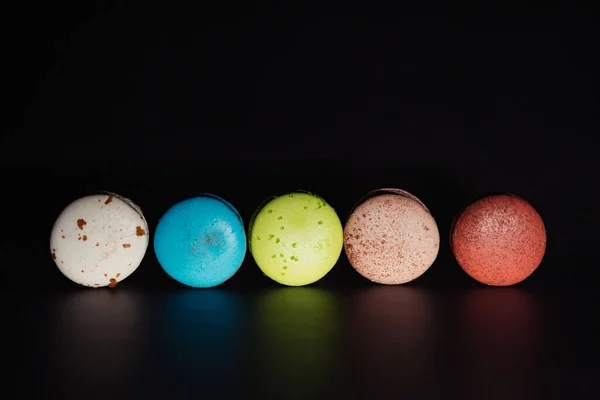 row of multi-colored macaroon cakes on a black background