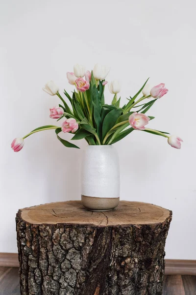 ceramic light vase with spring tulips on an unusual bedside table made of wood sawn