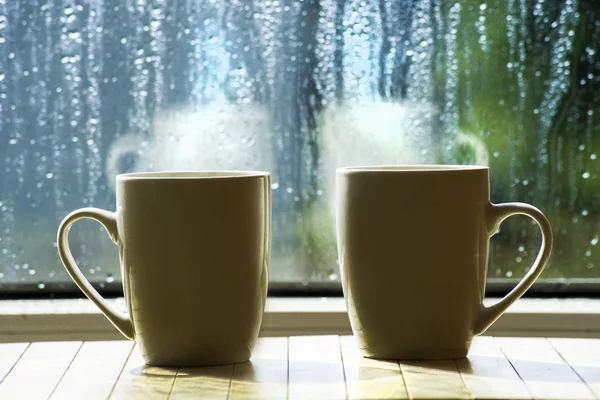 Две Чашки Горячим Напитком Фоне Окна Капельками Дождя Размытым Фоном — стоковое фото
