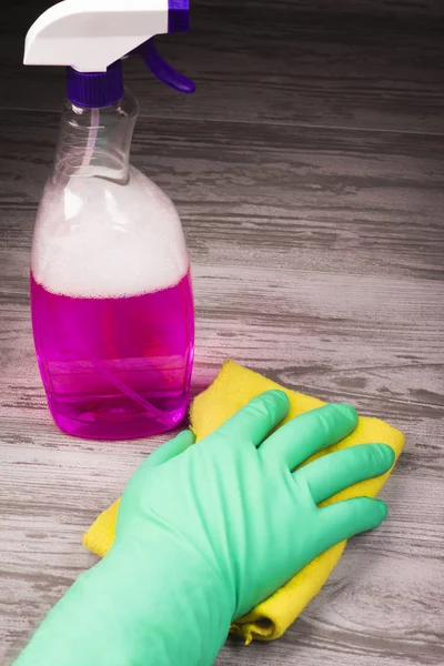 Items for cleaning, a hand in a green glove holding a yellow cloth on a background of a spray with a violet liquid