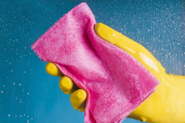 Bir bulaşık bezi holding - mavi bir arka plan üzerinde cam yıkama sarı eldiven El
