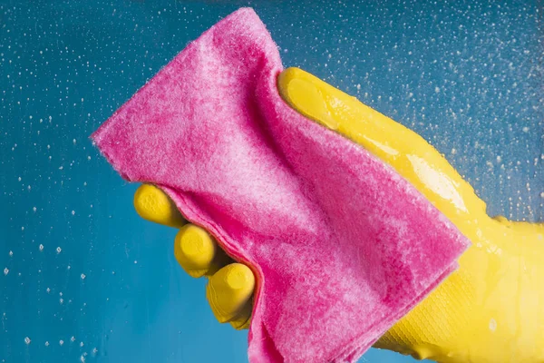 Bir bulaşık bezi holding - mavi bir arka plan üzerinde cam yıkama sarı eldiven El