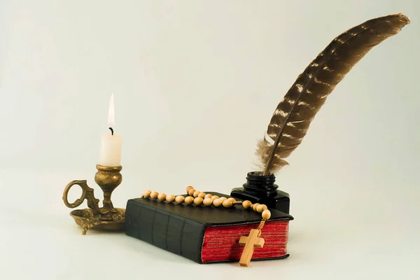 Book with a rosary and an inkwell with a pen, and a lit candle in the candlestick