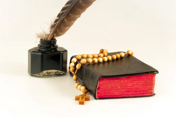 Book with a rosary, and an inkwell with a bird feather on a white background isolated