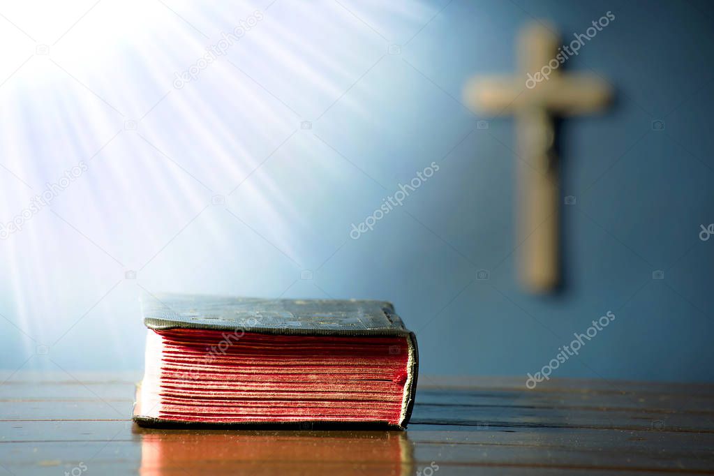 Book on the table in the rays of light with a crucifix in the background