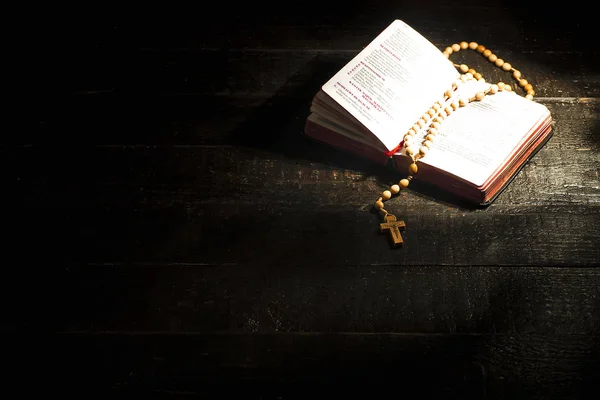 A bright open book with a rosary on dark boards — Stock Photo, Image