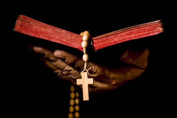 Hand holding an open book with a rosary, isolated on a black bac
