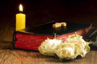 Eski kitap, solmuş güller, sarı bir mum ve bir haç kitap
