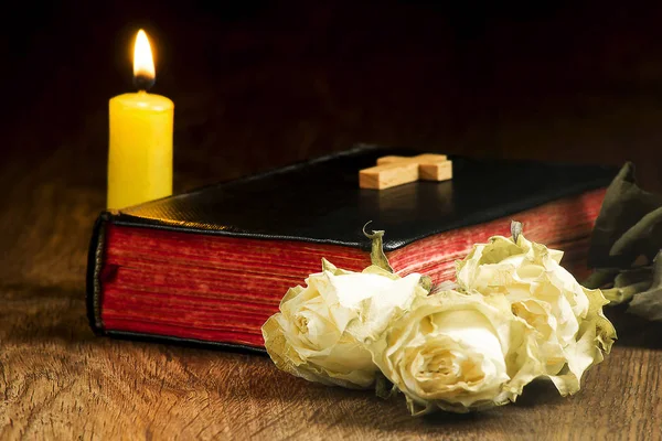 Eski kitap, solmuş güller, sarı bir mum ve bir haç kitap