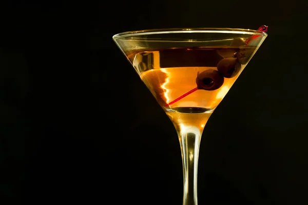 Um copo de martini com azeitonas verdes sobre um fundo preto — Fotografia de Stock