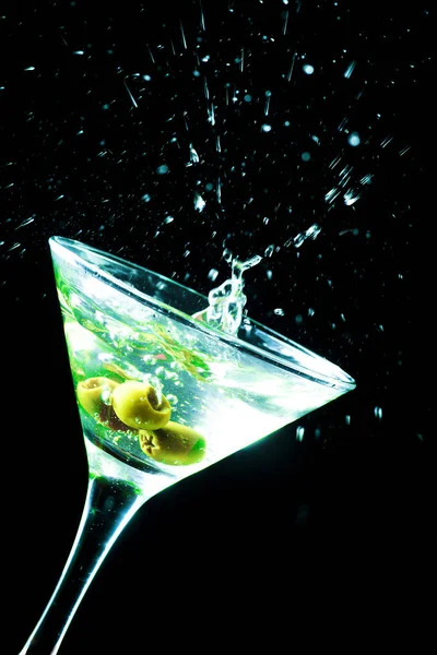 Um copo de martini com azeitonas verdes sobre um fundo preto — Fotografia de Stock