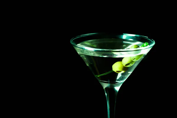 A martini glass with green olives on a black background