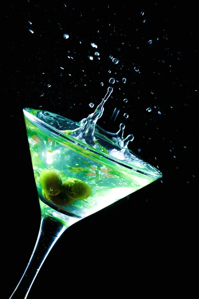 Um copo de martini com azeitonas verdes sobre um fundo preto — Fotografia de Stock