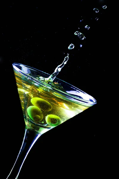 A martini glass with green olives on a black background — Stock Photo, Image