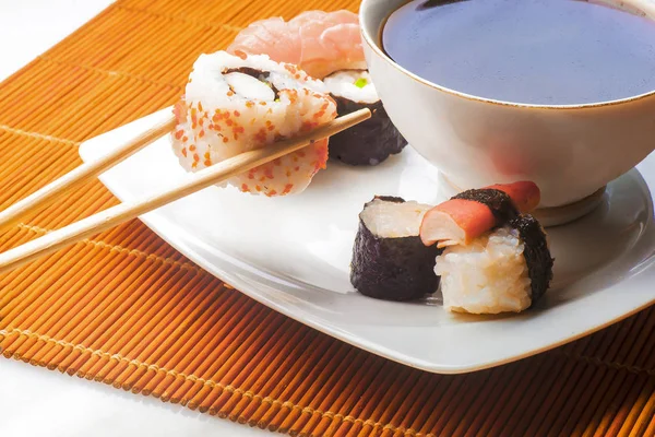 Sushi held in chopsticks over a bowl with sauce on a white backg — Stock Photo, Image