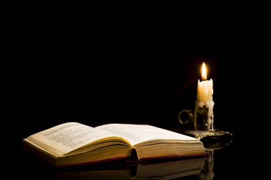 Siyah bir arka plan üzerinde izole açık bir kitap içinde bir mum ile