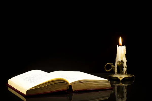 An open book isolated on a black background with a candle in the