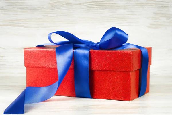 Красная подарочная коробка с голубой лентой на фоне винтажной доски — стоковое фото