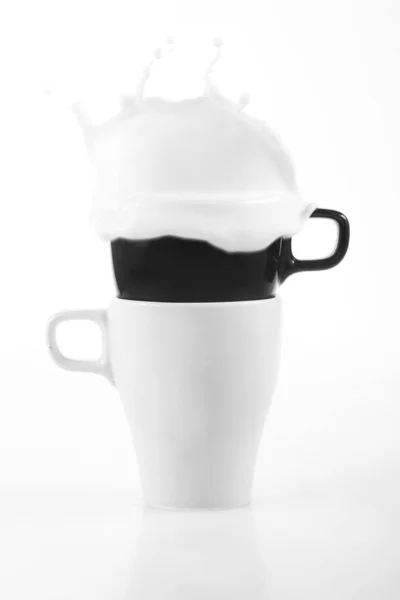 Caneca branca e caneca preta com leite em um fundo branco — Fotografia de Stock