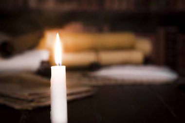 Bulanık parşömenlerin arka planına karşı yanan bir mum, kitaplar