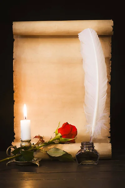 Pergamena di pergamena antica, rosa rossa, piuma e candela accesa Immagine Stock