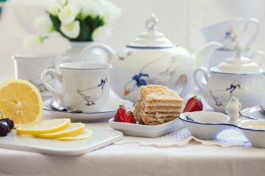 Lüks porselen çay seti ile bir bardak, Çaydanlık, süngerimsi pasta plaka ile beyaz masa örtüsü üzerinde şekerlik