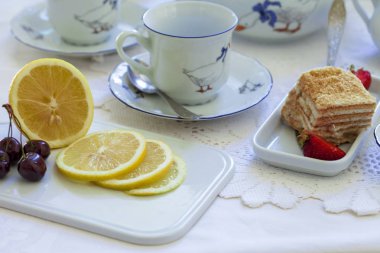 Lüks porselen çay seti ile bir bardak, Çaydanlık, süngerimsi pasta plaka ile beyaz masa örtüsü üzerinde şekerlik