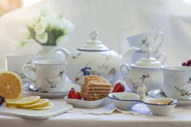 Lüks porselen çay seti ile bir bardak, Çaydanlık, süngerimsi pasta plaka ile beyaz masa örtüsü üzerinde şekerlik